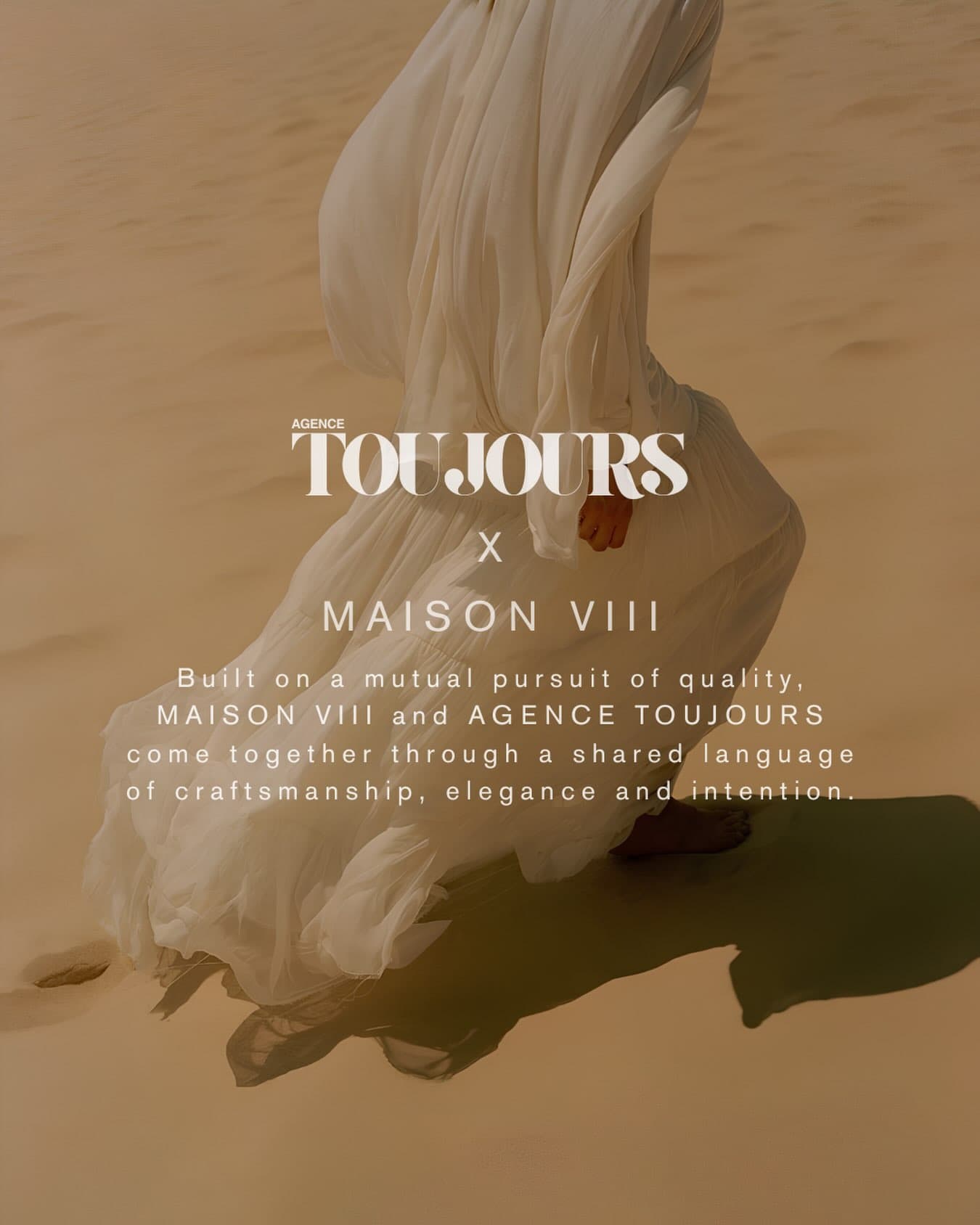 A figure in flowing white fabric walks across sand dunes