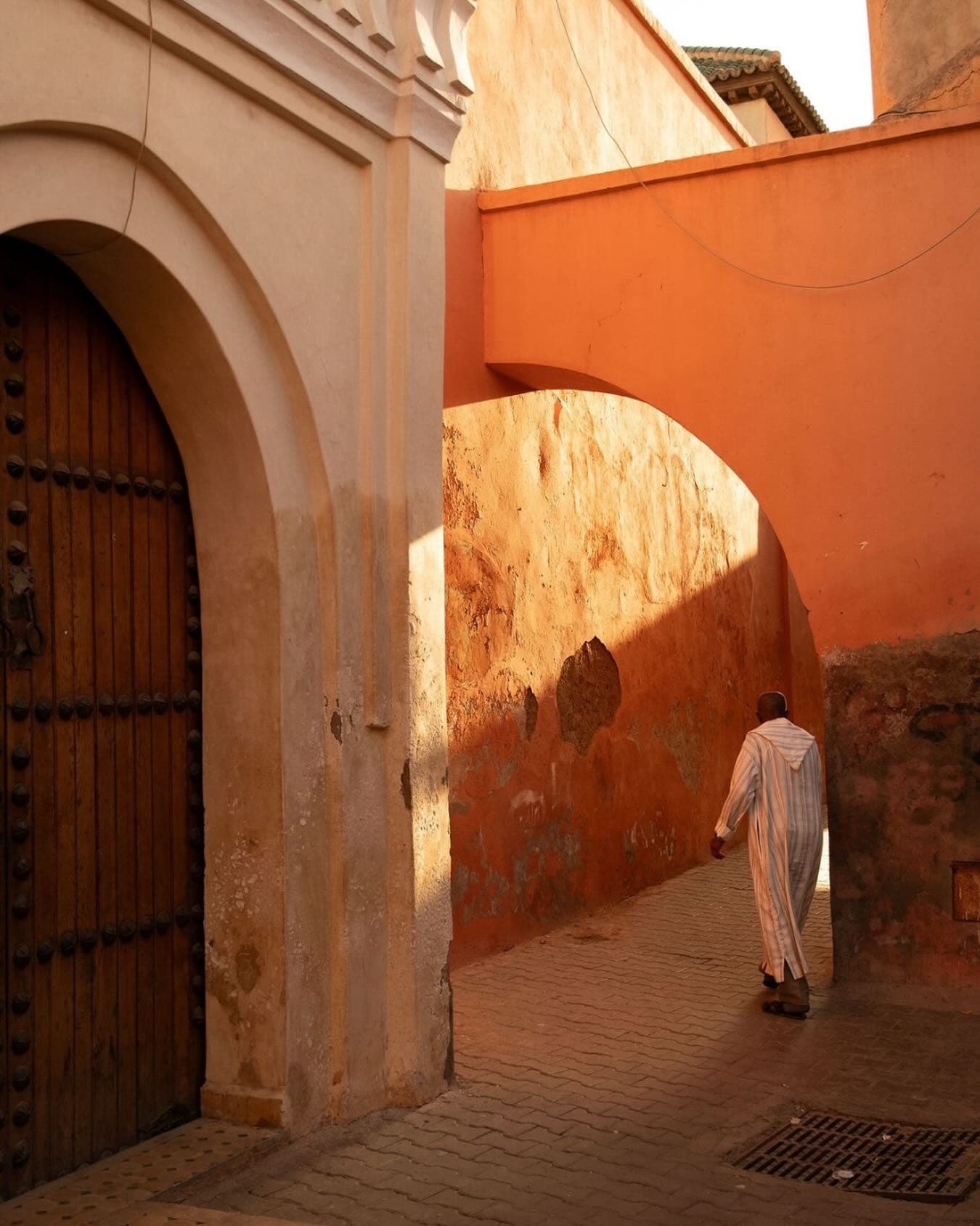 A man in a striped djellaba walks through a sunlit arcade in the Marrakech medina