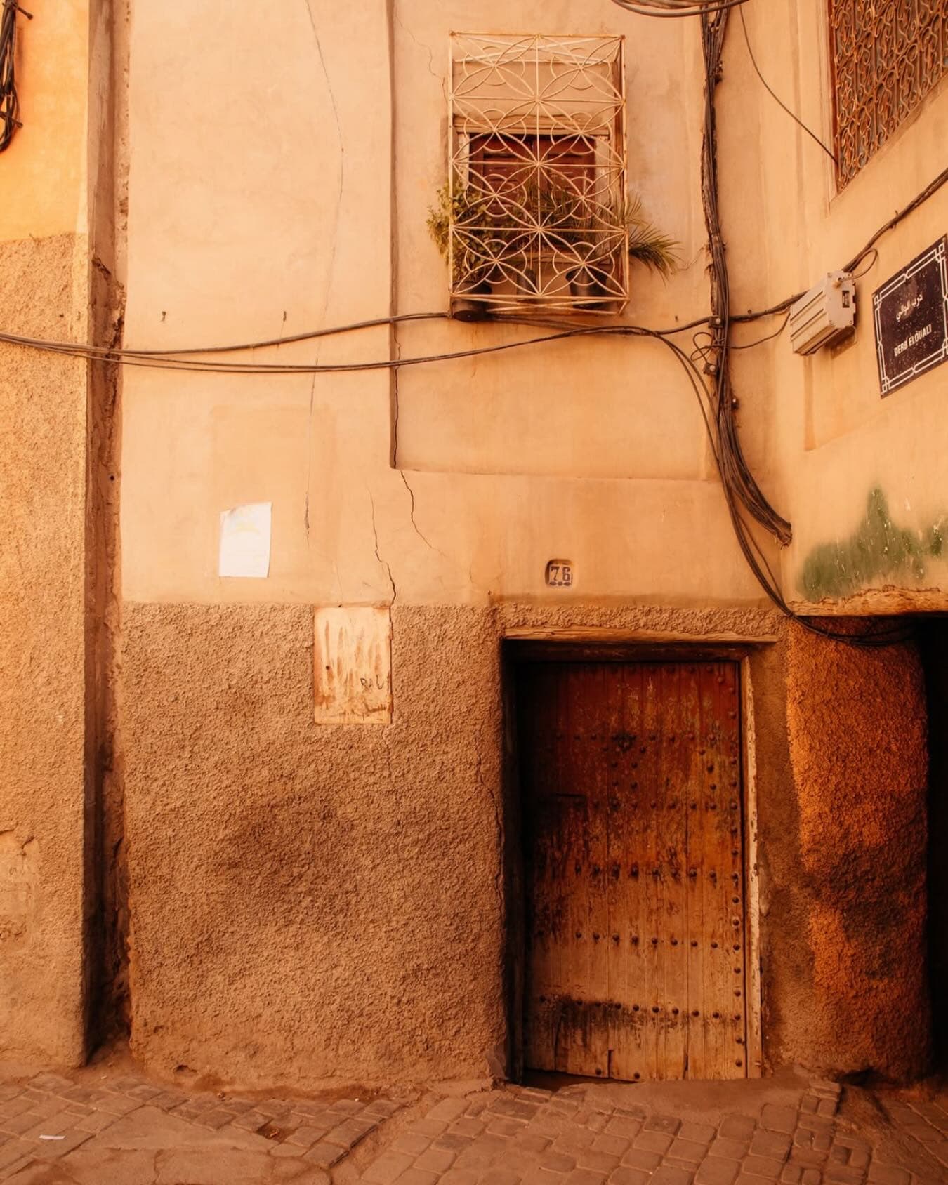An old wooden door below an iron window grille, in golden afternoon light