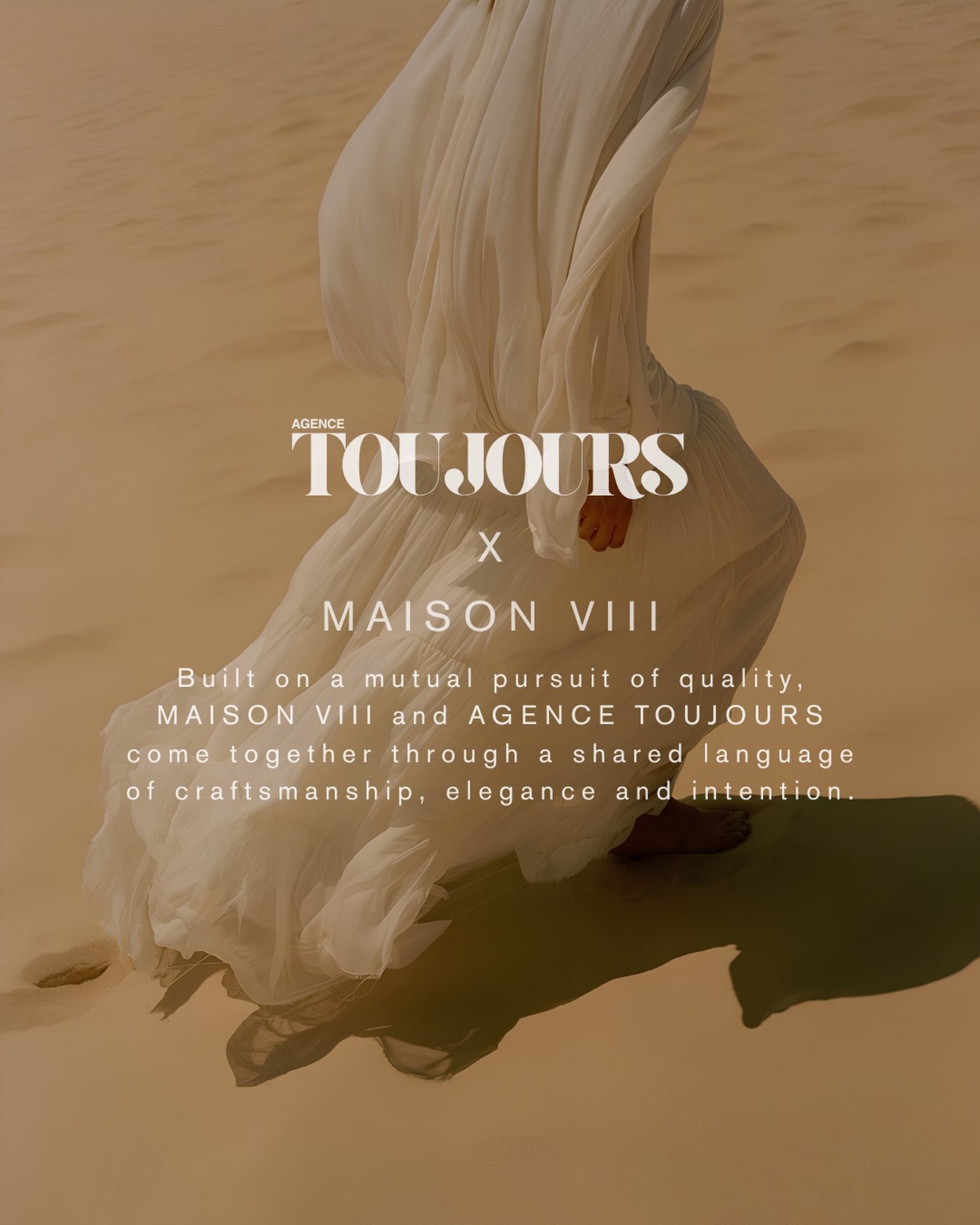 A figure in flowing white fabric walks across sand dunes